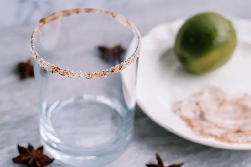 Empty cocktail glass with cinnamon sugar rim next to lime wedge and spices