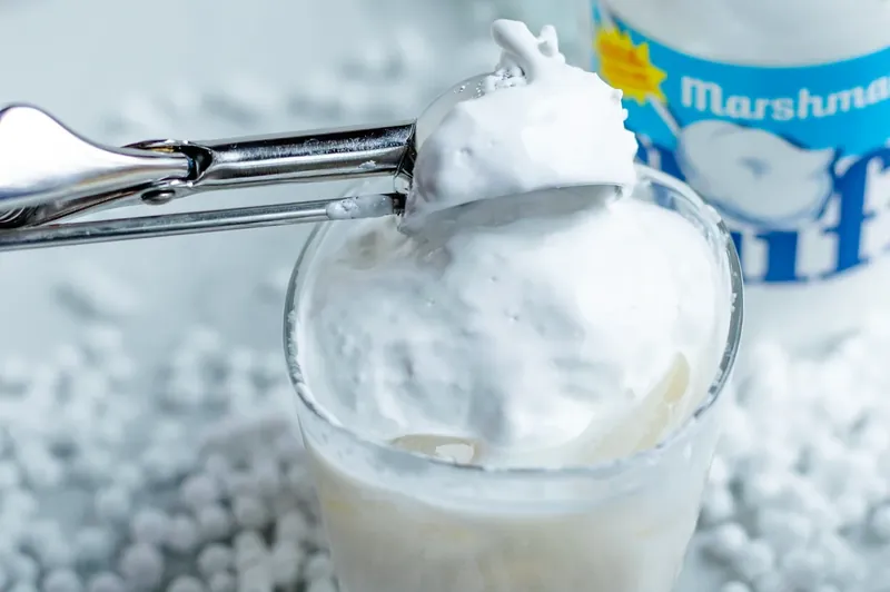Large scoop of marshmallow fluff being added to cocktail glass with ice cream scoop