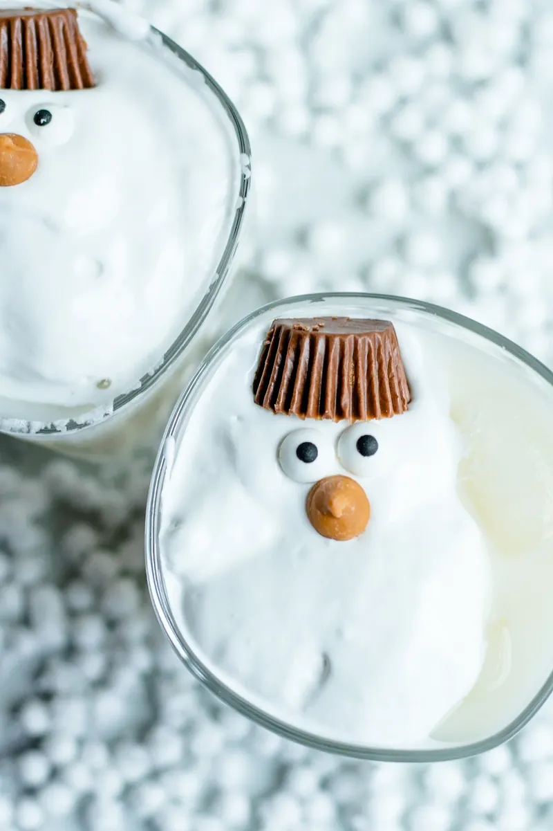 Two melted snowman margaritas with marshmallow fluff, candy eyes, and Reese's peanut butter cup hats