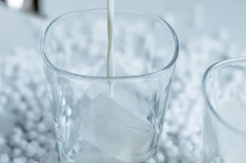 Clear cocktail glass being filled with ice cubes for melted snowman margarita
