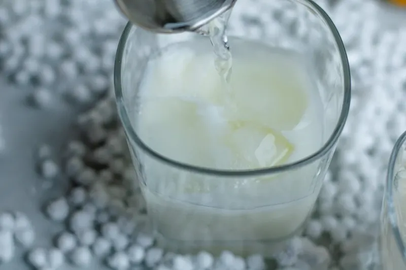 Cocktail ingredients being poured and mixed in ice-filled glass for snowman margarita