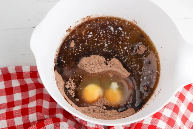 Mixing chocolate cake mix batter with eggs and butter in white bowl