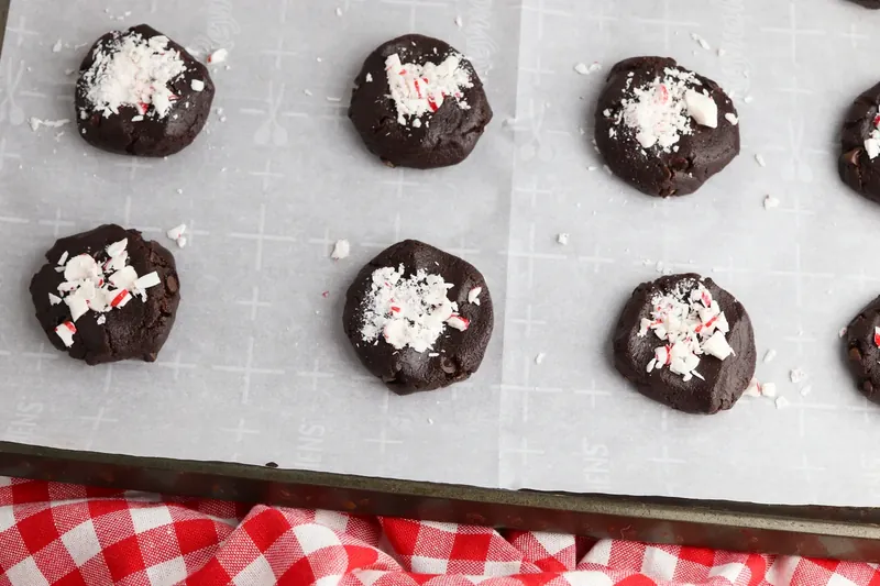 Shaped cookie dough balls topped with crushed peppermint on baking sheet