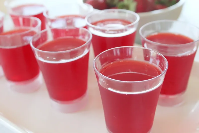 Red jello mixture poured into clear plastic shot cups on white tray