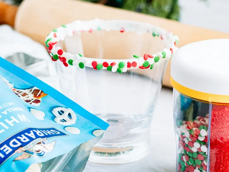 Cocktail glass rim being dipped in white chocolate and Christmas sprinkles