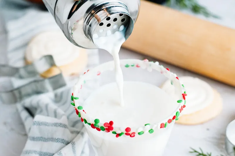Creamy white cocktail being poured into glass with Christmas sprinkle rim