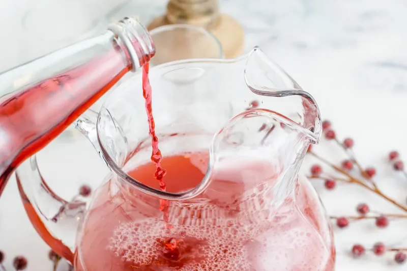 Pouring cranberry pomegranate juice into glass pitcher for margarita punch