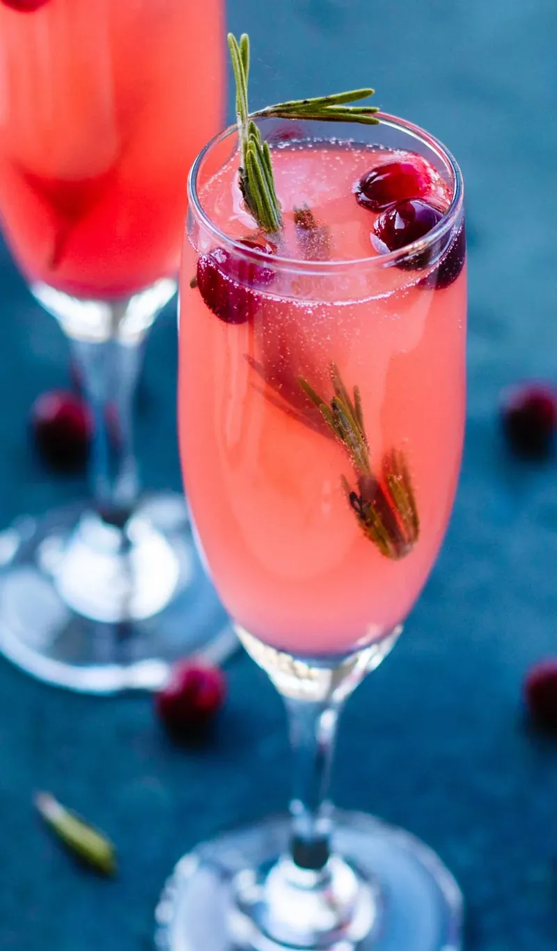 Vanilla cranberry mimosa in champagne flute garnished with fresh cranberries and rosemary sprig
