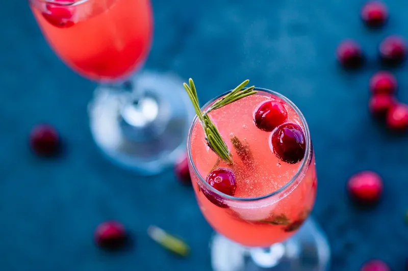 Garnishing vanilla cranberry mimosa with fresh cranberries and rosemary sprig