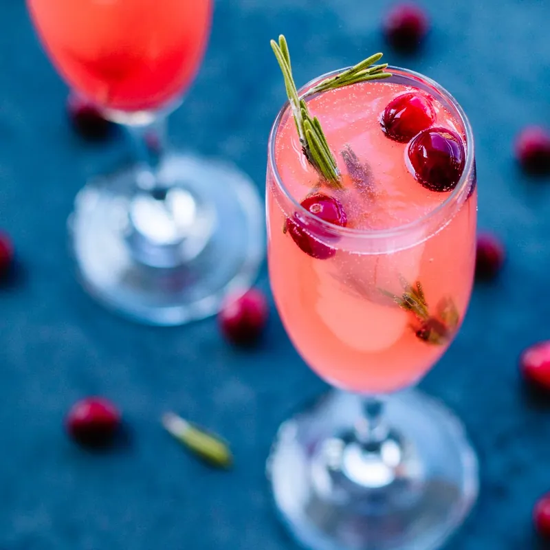 Perfect vanilla cranberry mimosa in champagne flute with cranberry and rosemary garnish