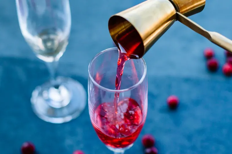 Pouring cranberry juice mixture into champagne flute for vanilla cranberry mimosa