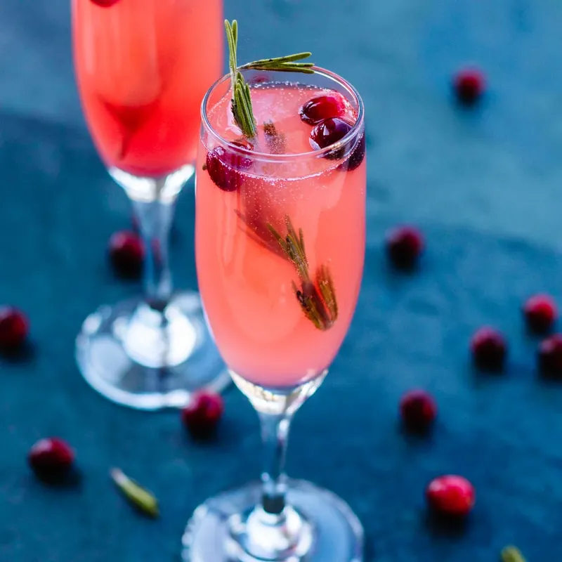 Styled vanilla cranberry mimosa with scattered cranberries on blue background