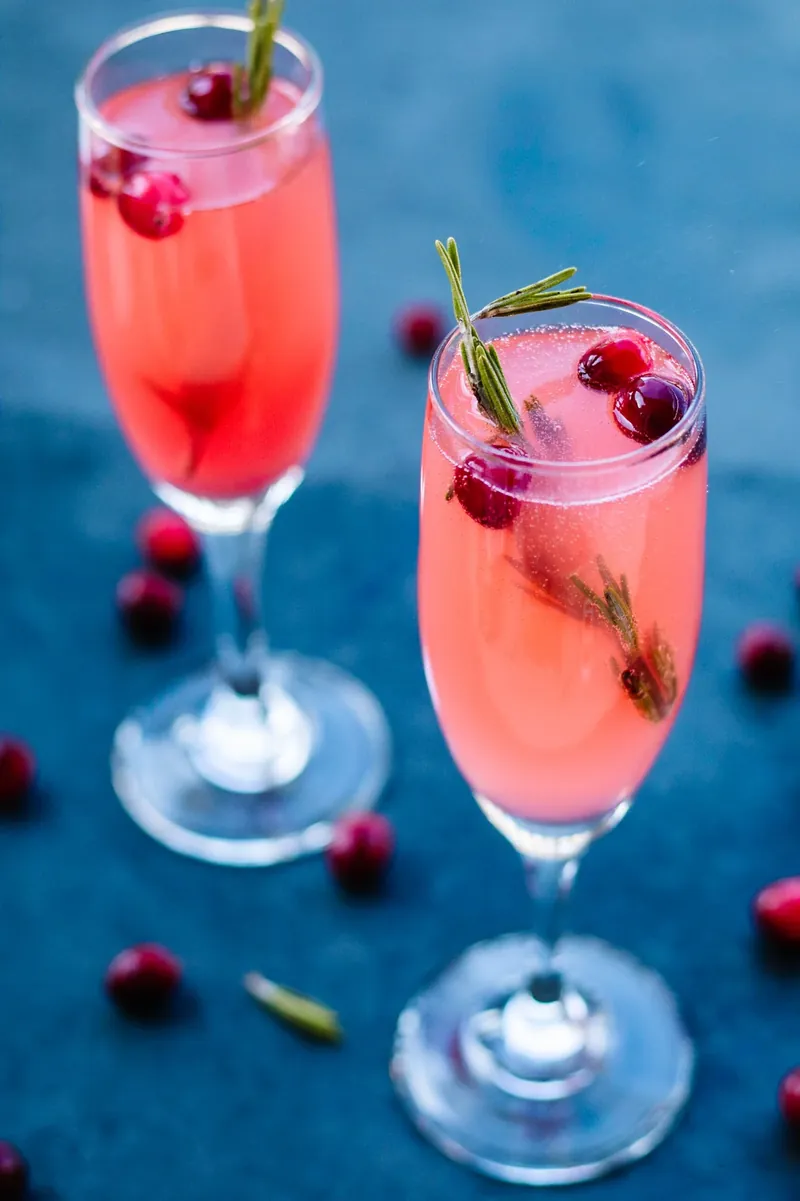 Two vanilla cranberry mimosas in champagne flutes with cranberry and rosemary garnish