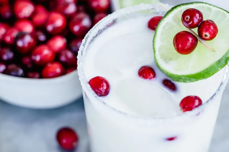Completed White Christmas Margarita with lime garnish and cranberries in peppermint-rimmed glass
