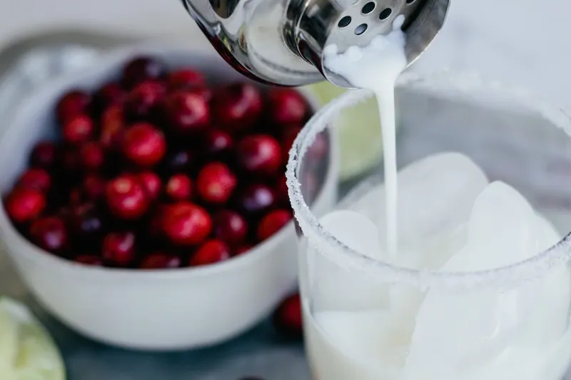 Pouring margarita mixture into glass filled with ice and cranberries