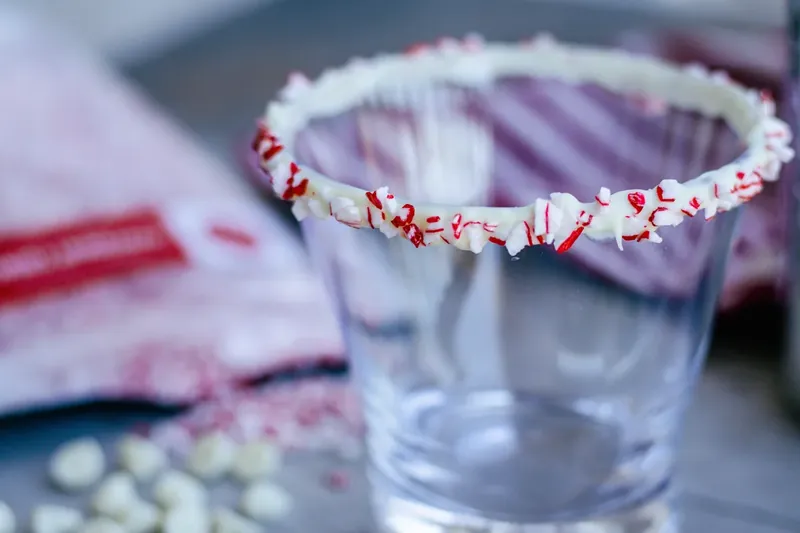 Cocktail glass rim being dipped in melted white chocolate and crushed peppermints