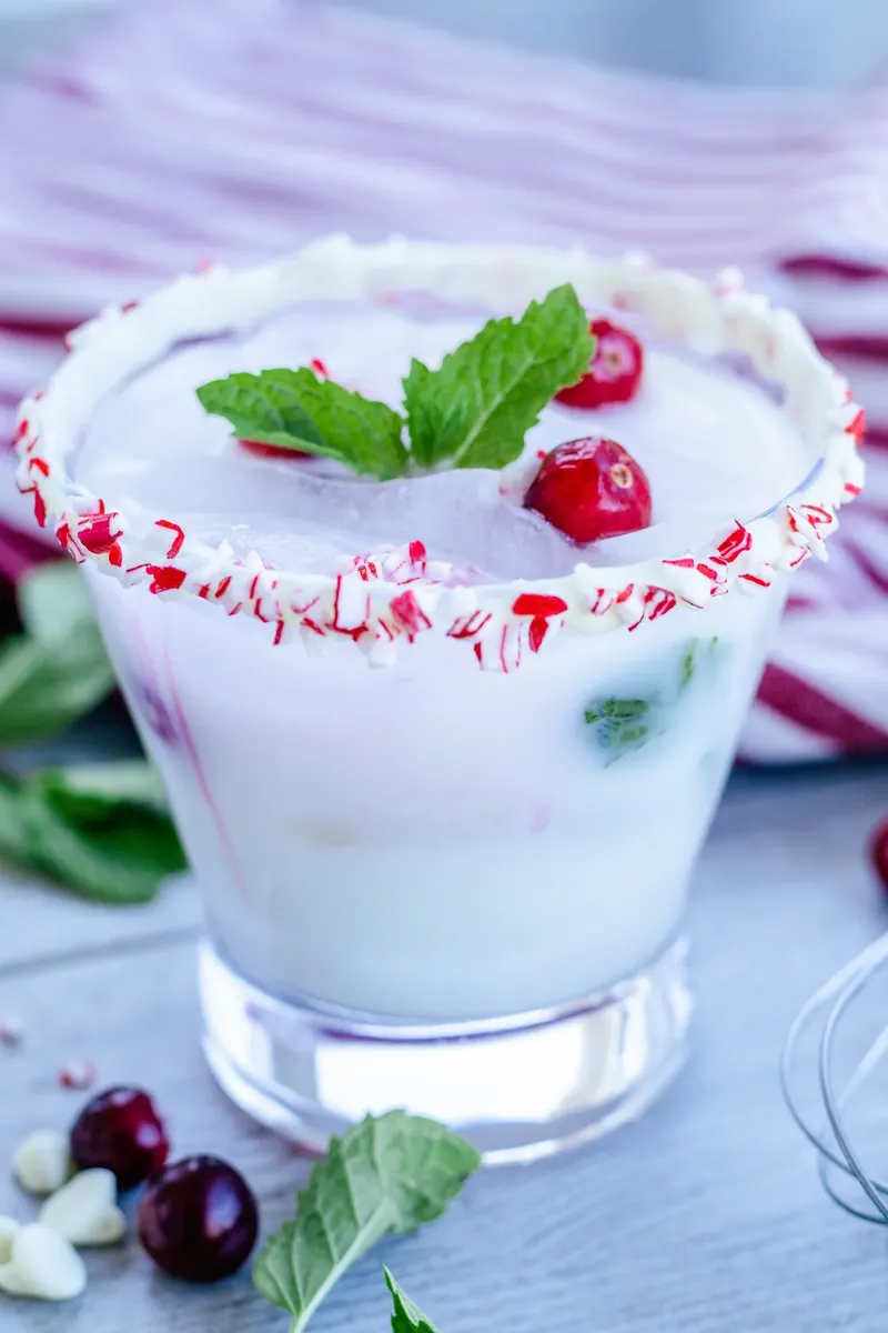 White Christmas mojito with peppermint rim garnish, cranberries and mint in frosted glass