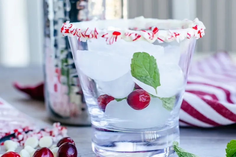 Glass being filled with ice, mint leaves and fresh cranberries layered throughout