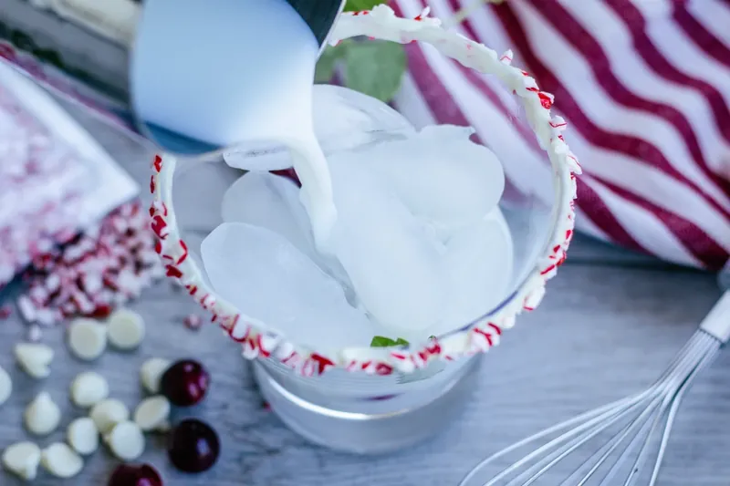 Pouring white mojito mixture into prepared glass with ice and garnishes