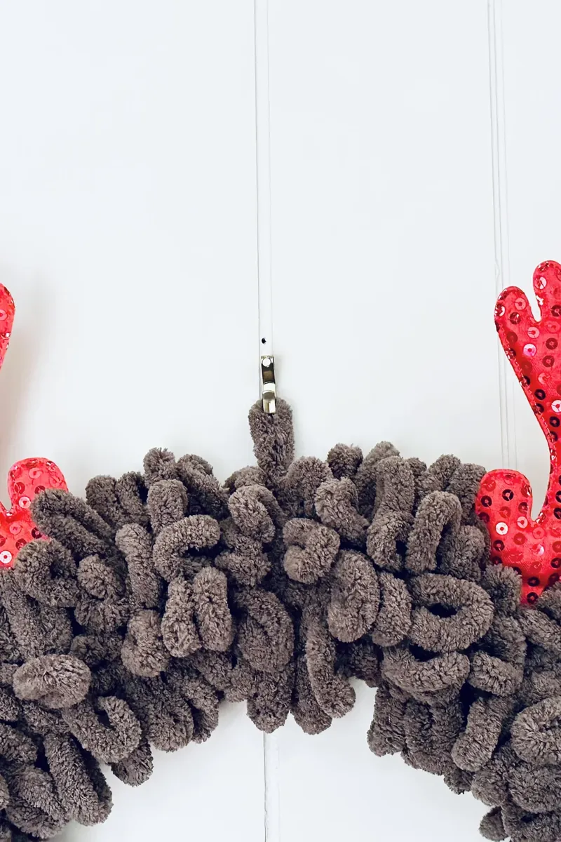 Close up view of fluffy taupe yarn texture on completed reindeer wreath with red accents