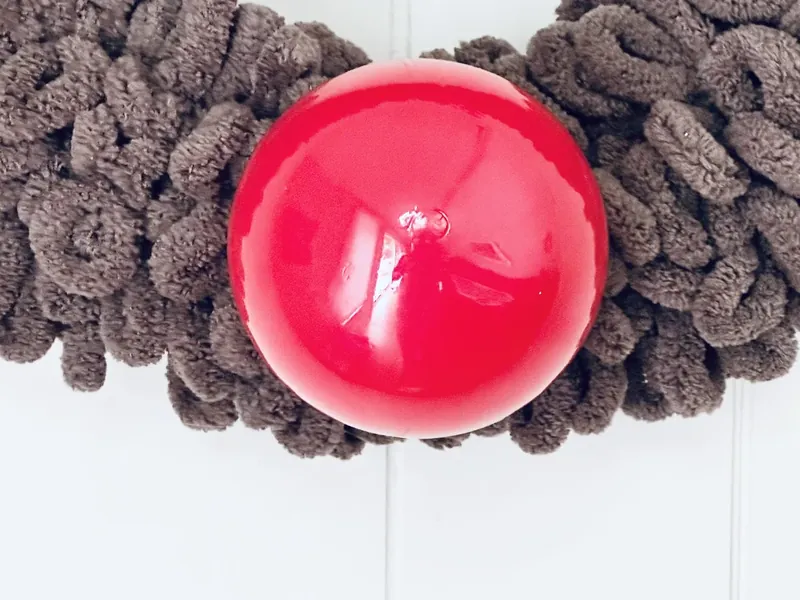 Red sequin antlers being hot glued to top of yarn wreath to create reindeer look