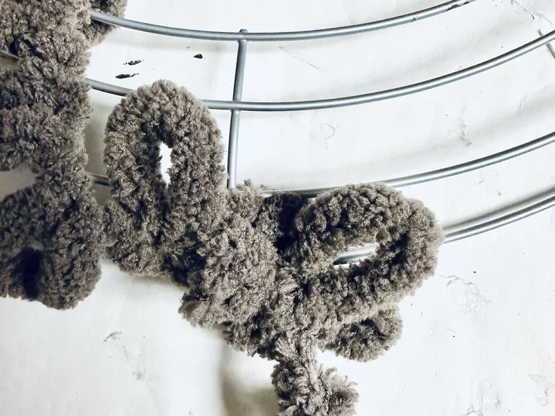 Taupe yarn being tied to wire wreath form to start wrapping process