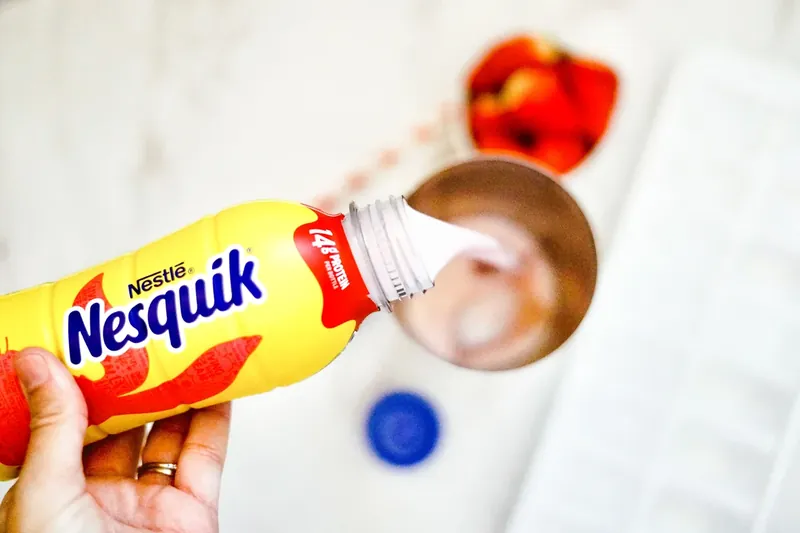 Strawberry milk being poured into cocktail shaker with other ingredients