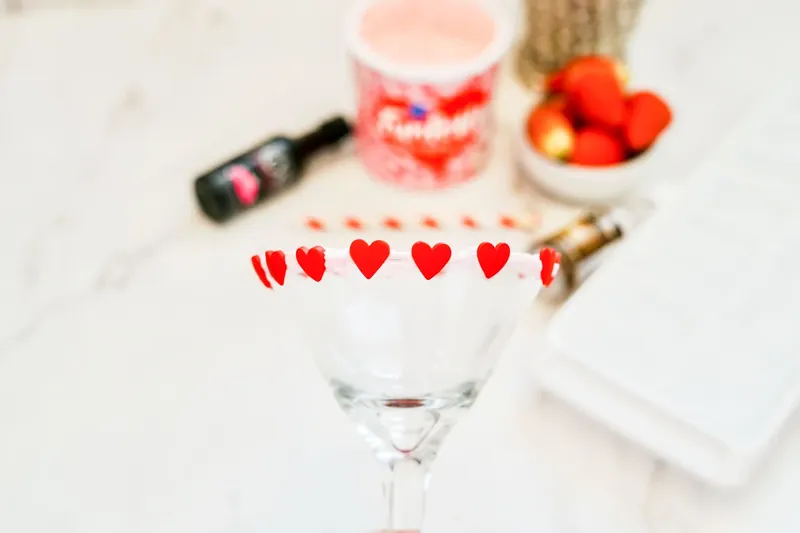 Red candy hearts being attached to frosted martini glass rim