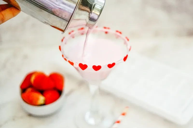Pink chocolate strawberry martini being poured into heart-decorated glass